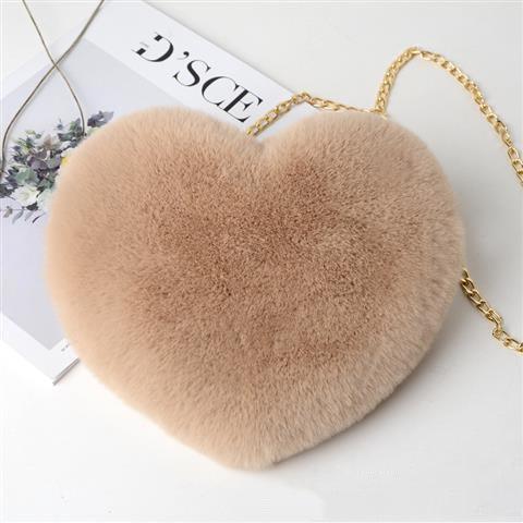 Beige heart-shaped fluffy handbag with gold chain strap on white surface