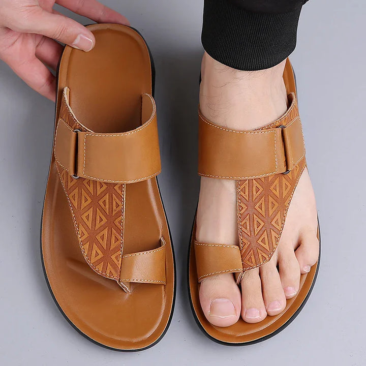 Tan brown men's open-toe leather sandals with geometric pattern on straps, one worn and one held