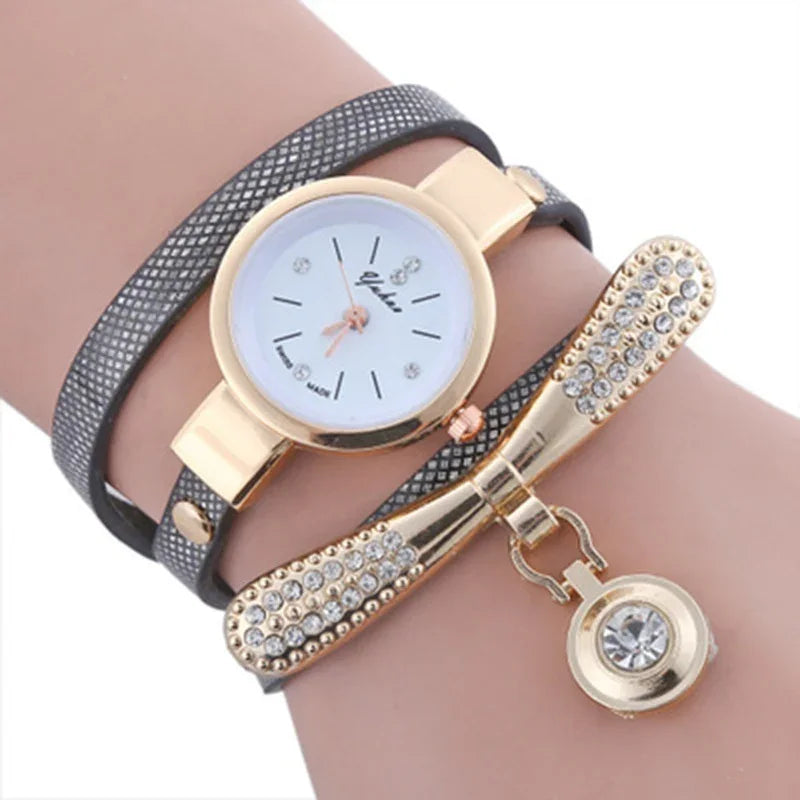 Elegant wristwatch with gold case and white dial, paired with black leather strap and rhinestone-studded gold bow bracelet
