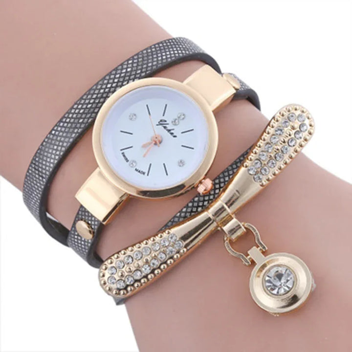 Elegant wristwatch with gold case and white dial, paired with black leather strap and rhinestone-studded gold bow bracelet