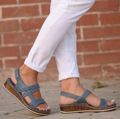Woman wearing blue wedge sandals with cork soles and white cropped pants walking on stone pavement