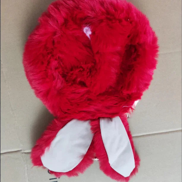 Red fluffy winter hat with white bunny ears on a beige surface