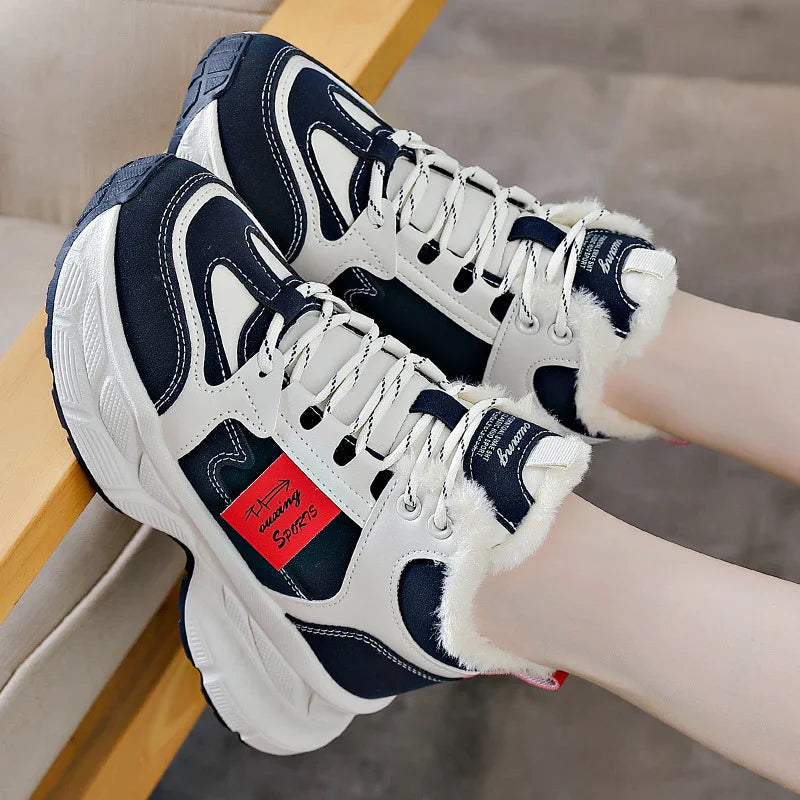White and black chunky sneakers with fur lining and red sports label, worn on feet indoors