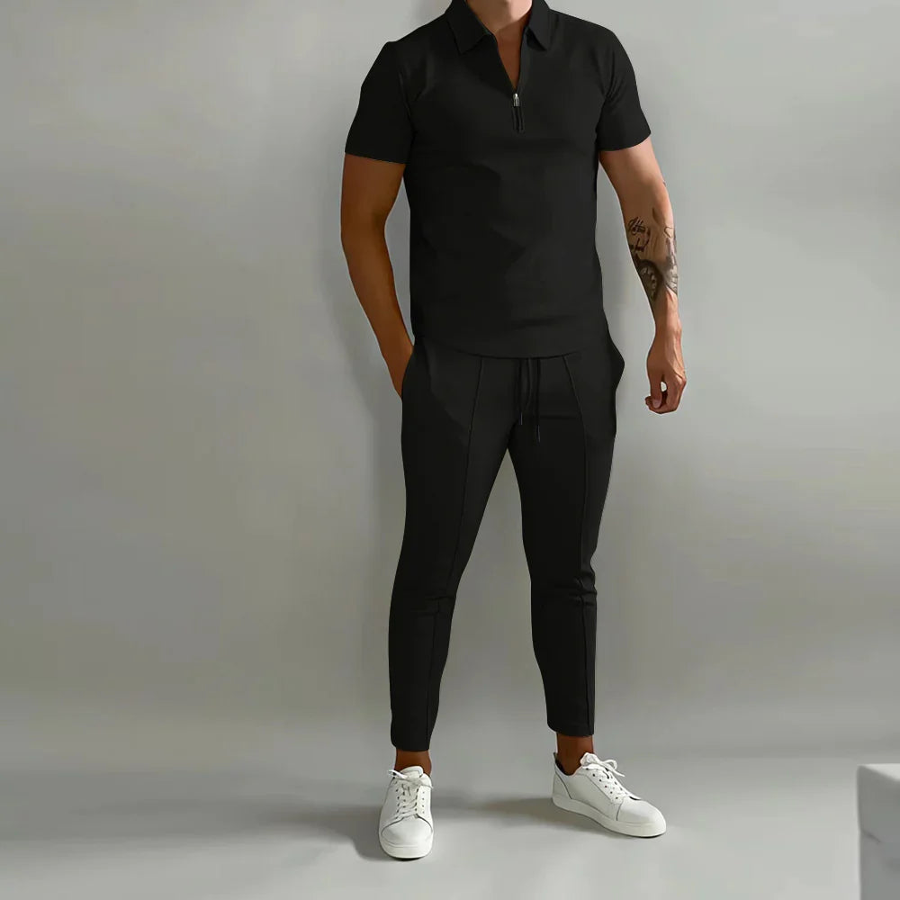 Man wearing black short-sleeve polo shirt and black jogger pants with white sneakers against gray background