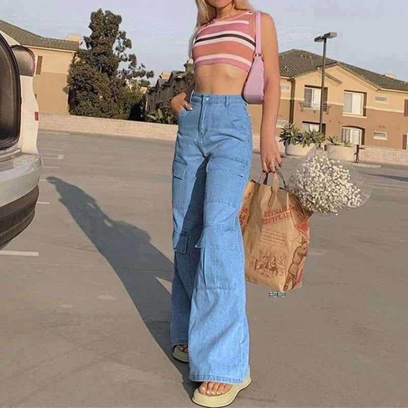 Woman in pink striped crop top and blue wide-leg jeans holding paper bag with white flowers in sunny parking lot