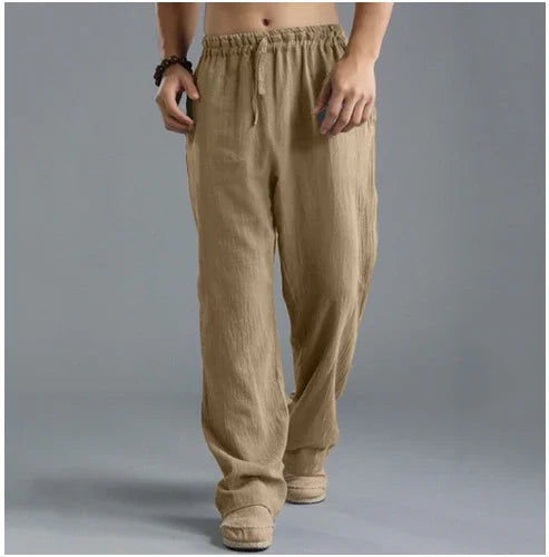 Man wearing loose beige linen pants with elastic waistband and drawstring on gray background