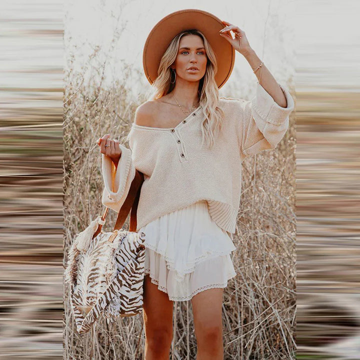 Woman wearing beige off-shoulder sweater, layered white skirt, brown hat, holding zebra print bag in dry grass field