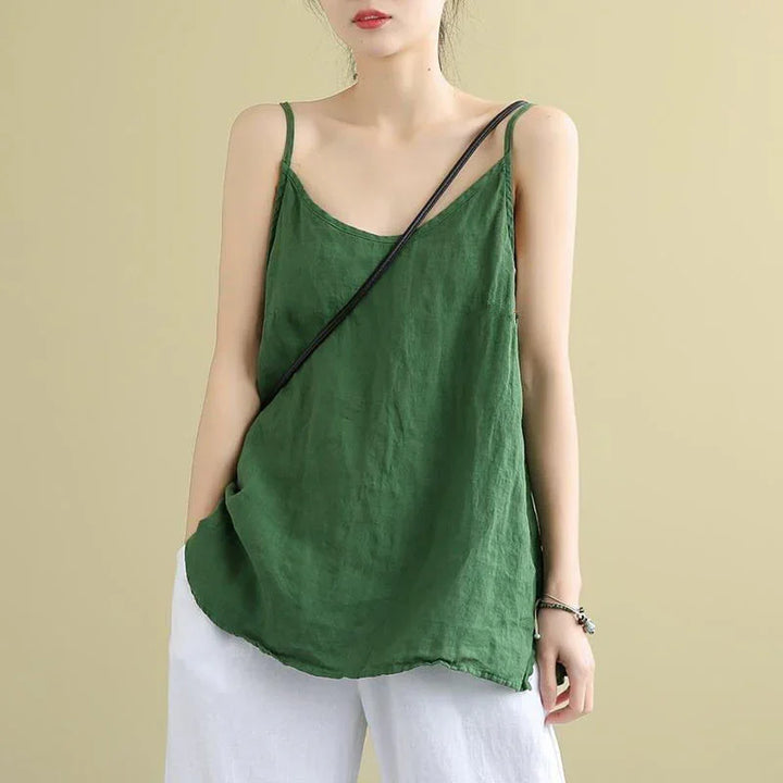Woman wearing green sleeveless linen top and white pants with black crossbody bag strap