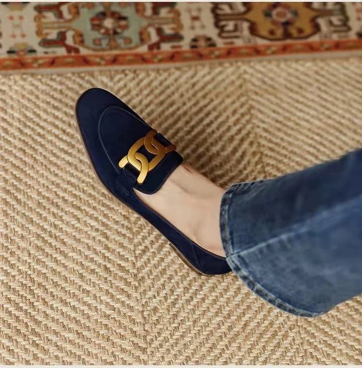 navy blue suede loafer with gold chain detail worn with blue jeans on woven rug