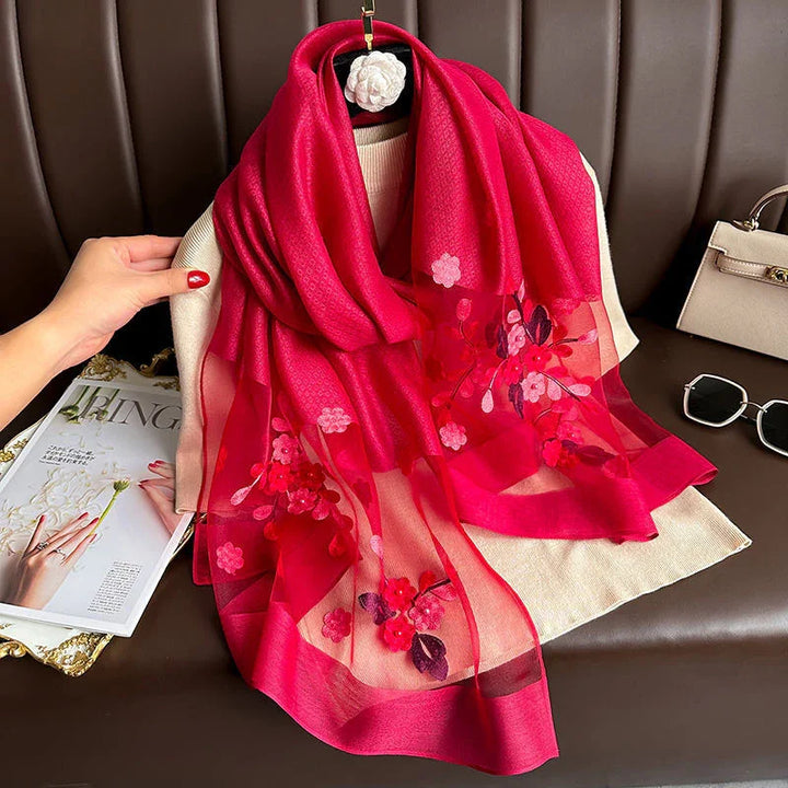 Bright red floral embroidered lightweight scarf displayed on beige fabric with a hand and fashion magazine nearby