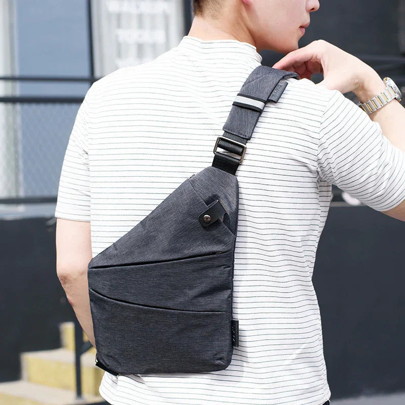 Man wearing a striped white t-shirt carrying a dark gray sling backpack outdoors