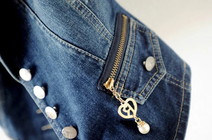 Close-up of blue denim jacket sleeve with silver buttons and gold zipper pull featuring heart and pearl charm