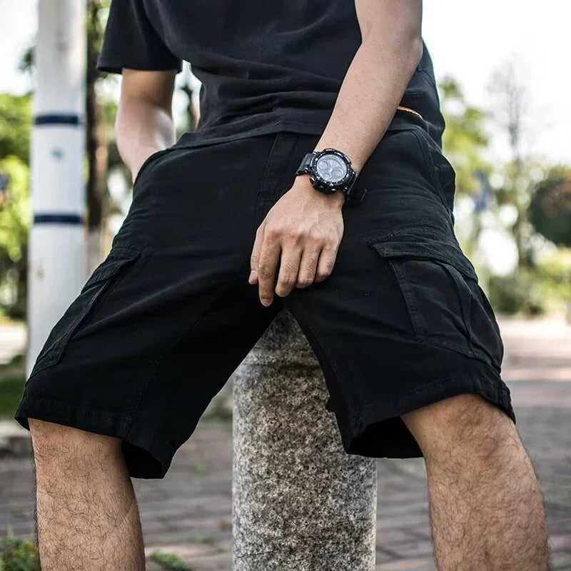 Man wearing black cargo shorts and black watch sitting outdoors on a stone post