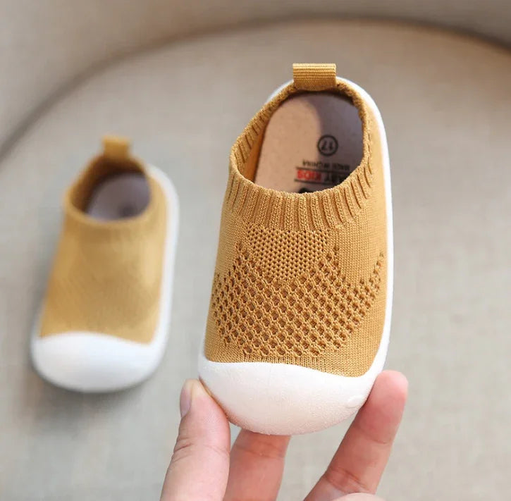 Hand holding mustard yellow knit baby shoe with white rubber toe and textured pattern