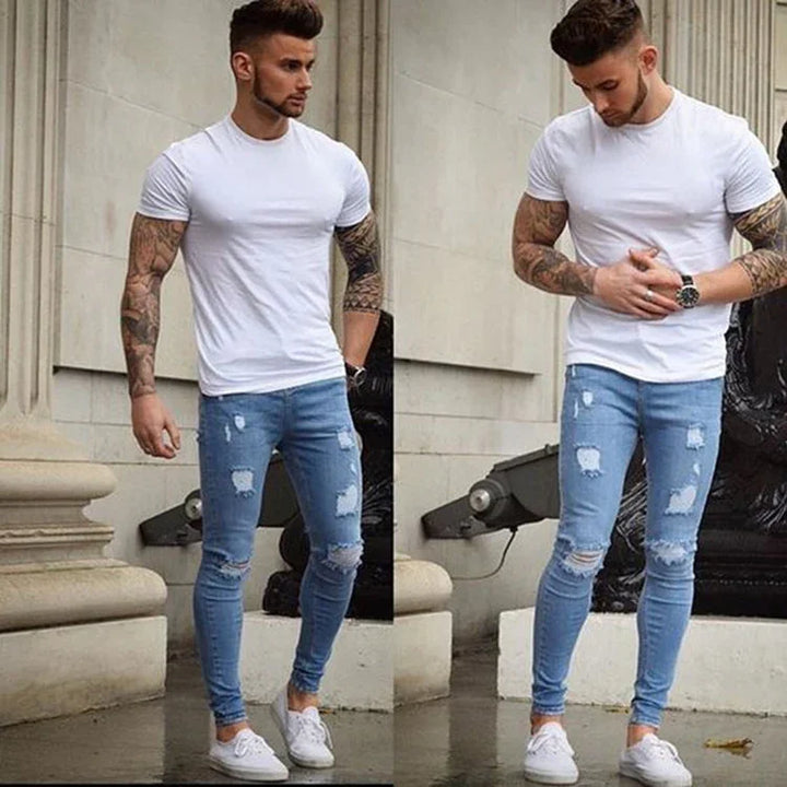 man wearing fitted white t-shirt and ripped skinny blue jeans with white sneakers standing outdoors