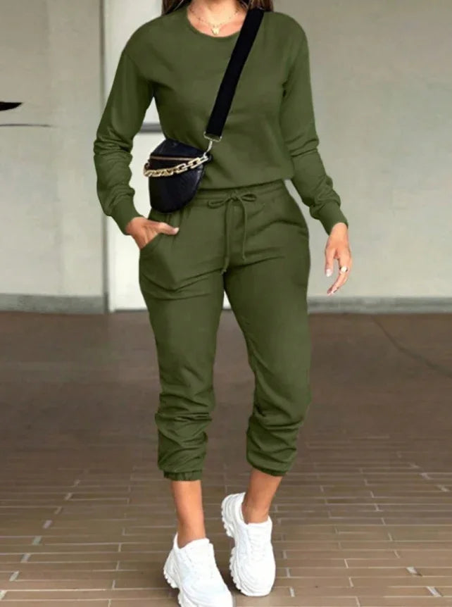 Woman wearing olive green long-sleeve jumpsuit with pockets, white sneakers, and black crossbody bag