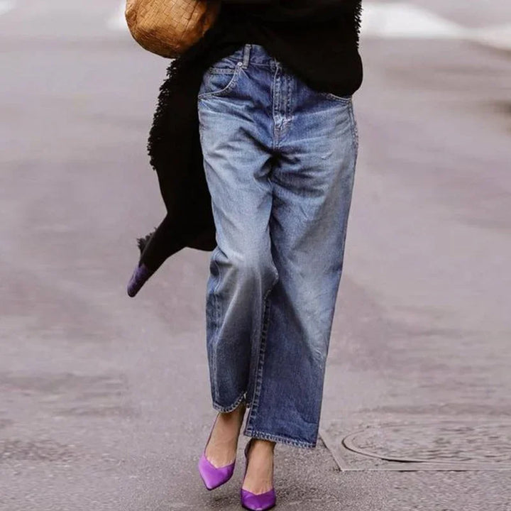 woman wearing wide-leg blue jeans and purple pointed heels walking on urban pavement