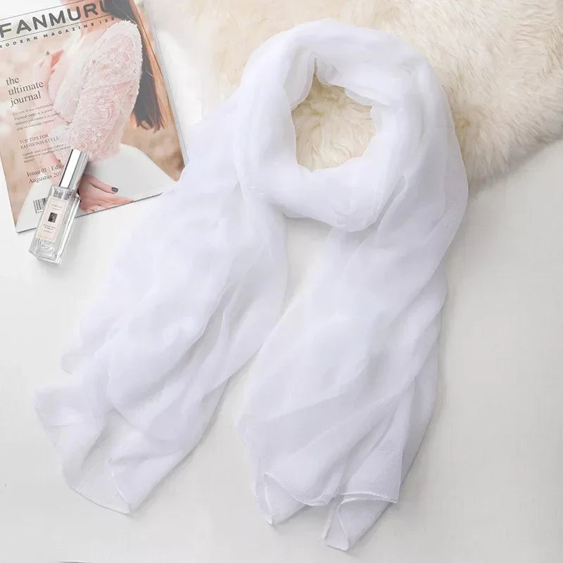 Elegant white chiffon scarf on a soft surface next to a fashion magazine and perfume bottle