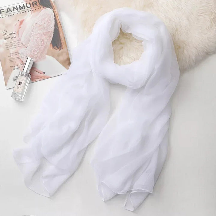 Elegant white chiffon scarf on a soft surface next to a fashion magazine and perfume bottle