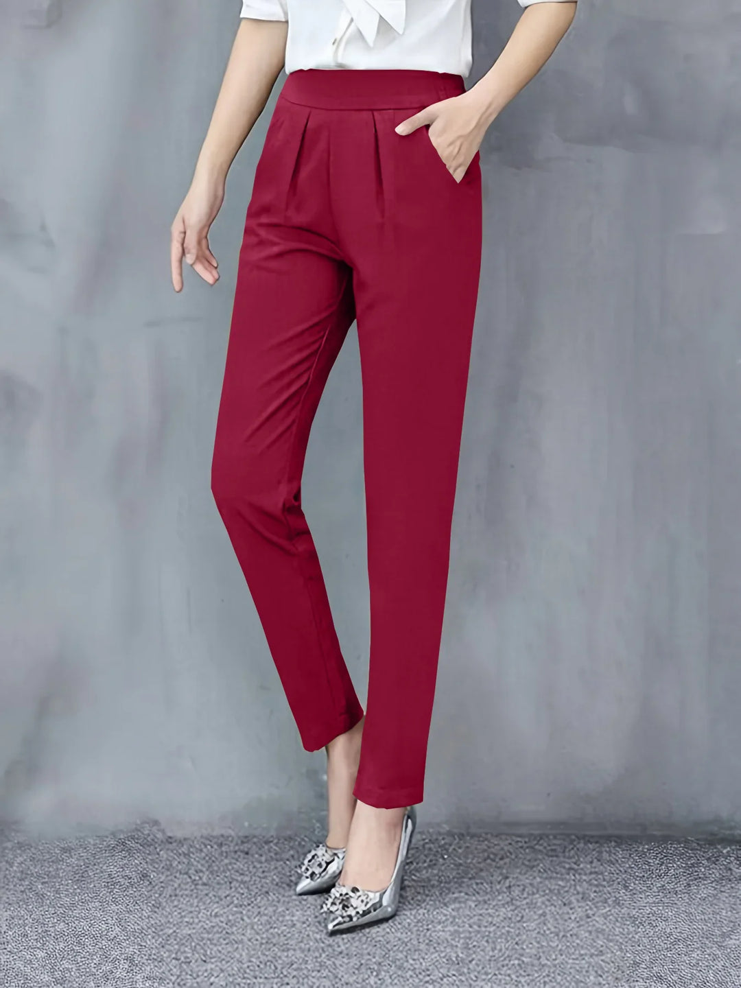 Woman wearing stylish red high-waisted trousers with pleats and silver pointed heels