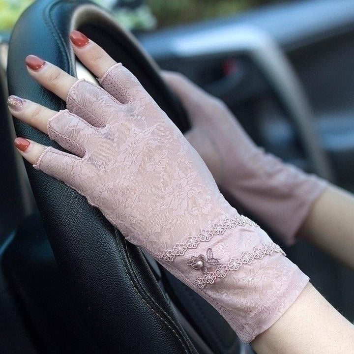 Pink lace fingerless gloves with floral pattern and bead decoration worn while holding a black car steering wheel