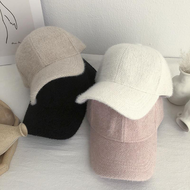 Four soft knitted baseball caps in beige, black, white, and pink displayed on a white surface