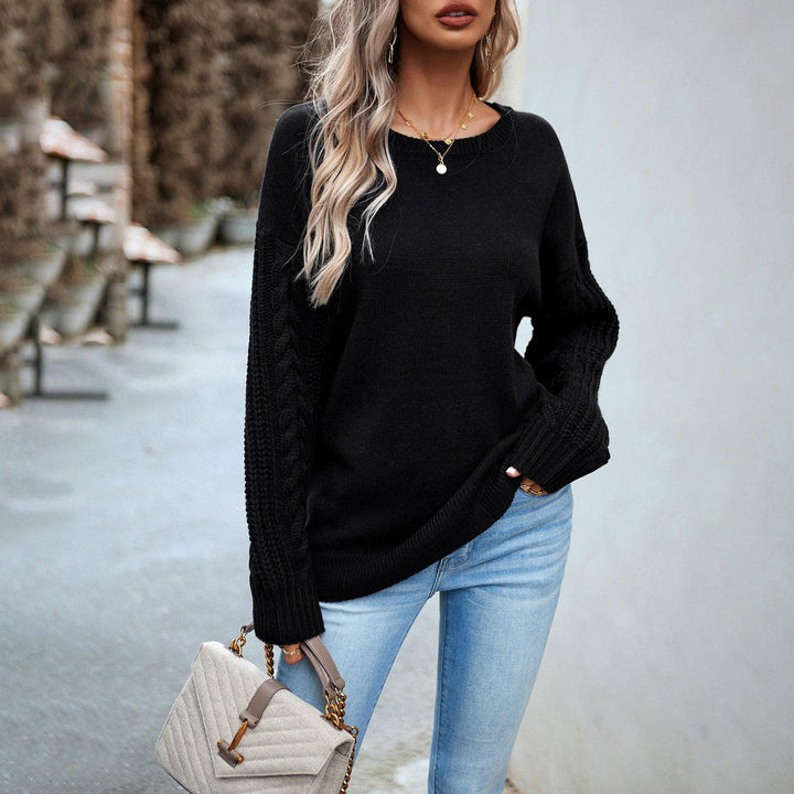 Woman wearing black cable knit sweater and light blue jeans holding beige handbag outdoors
