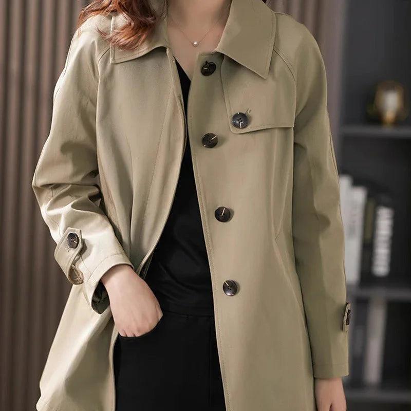 Woman wearing beige trench coat with large buttons over black outfit in indoor setting
