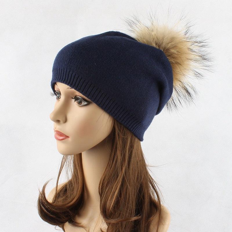 Navy blue knit beanie with a large beige faux fur pom-pom on a mannequin head with brown hair