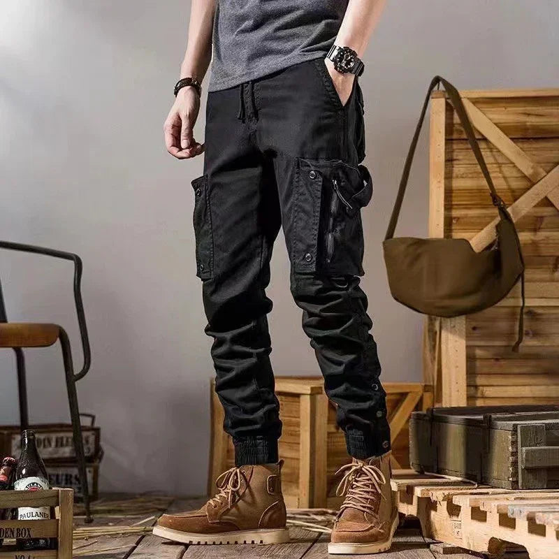 Man wearing black cargo jogger pants with front pockets and brown ankle boots in a wooden rustic room