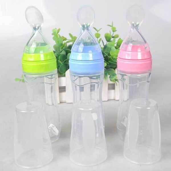 Three transparent baby feeding bottles with green, blue, and pink caps, set against a background of green plants