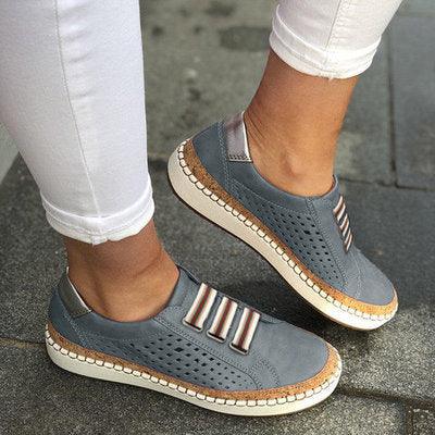 Close-up of stylish gray slip-on sneakers with perforated design and striped elastic bands worn with white pants outdoors