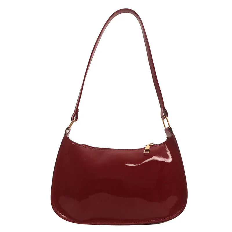 Shiny burgundy leather shoulder bag with gold zipper and single strap on white background