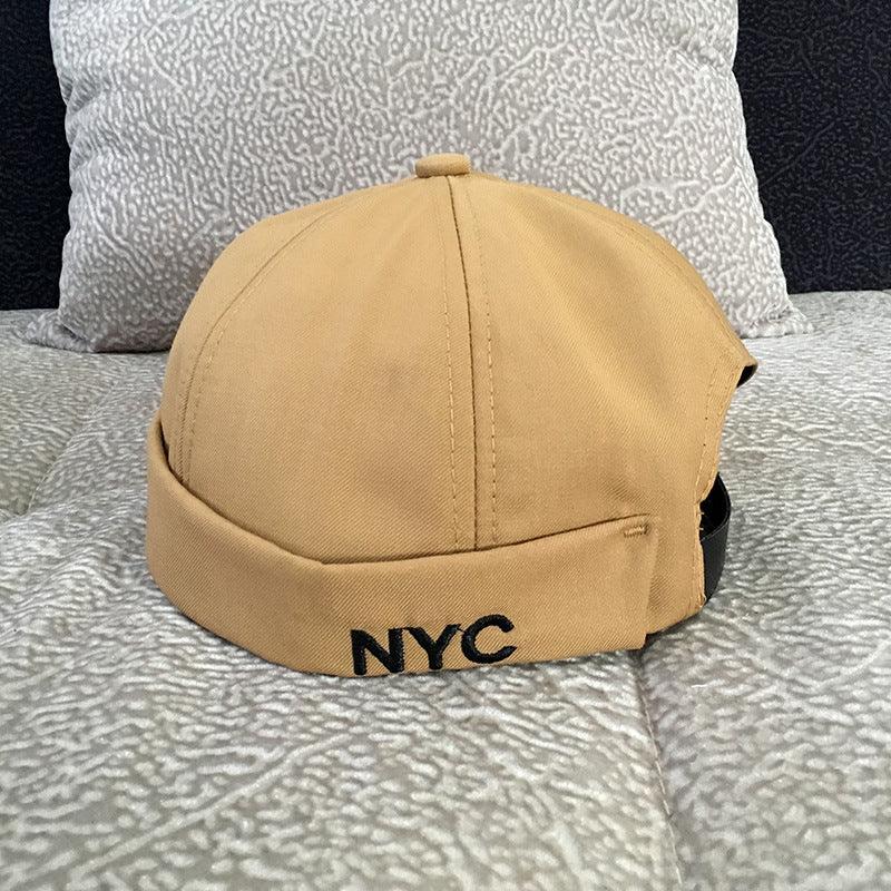 Beige cotton bucket hat with black stitched NYC logo on a patterned fabric surface