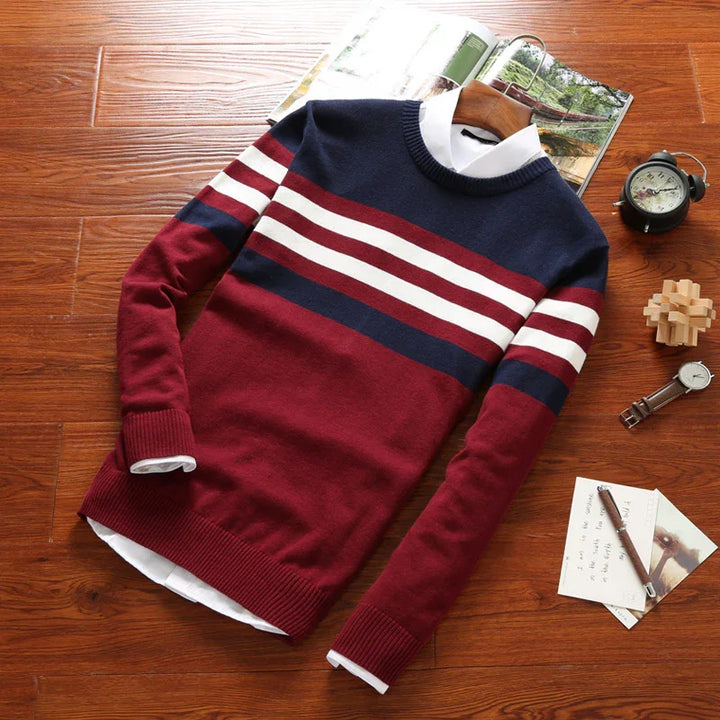 Men's crew neck striped sweater in burgundy, navy, and white on wooden floor with watch and notebook
