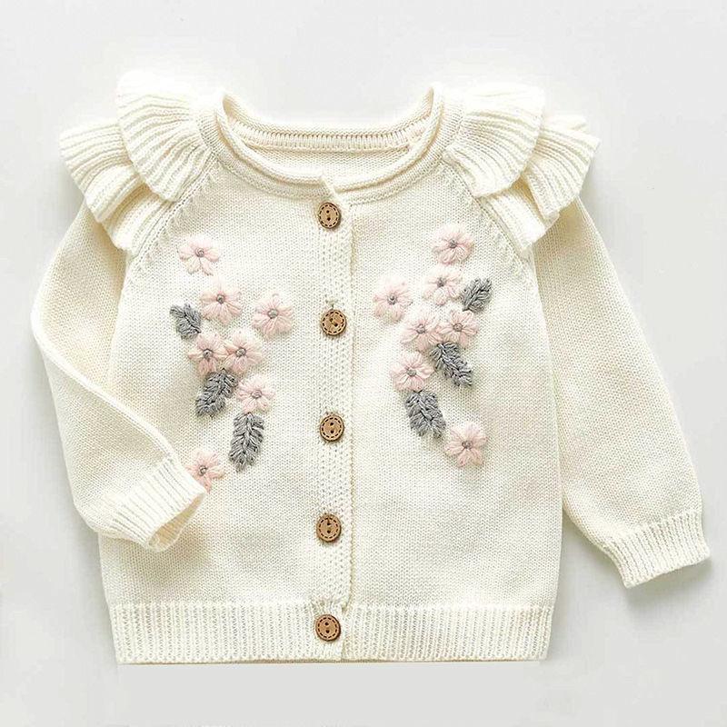Cream-colored baby cardigan with ruffled shoulders, pink flower and gray leaf embroidery, and wooden buttons