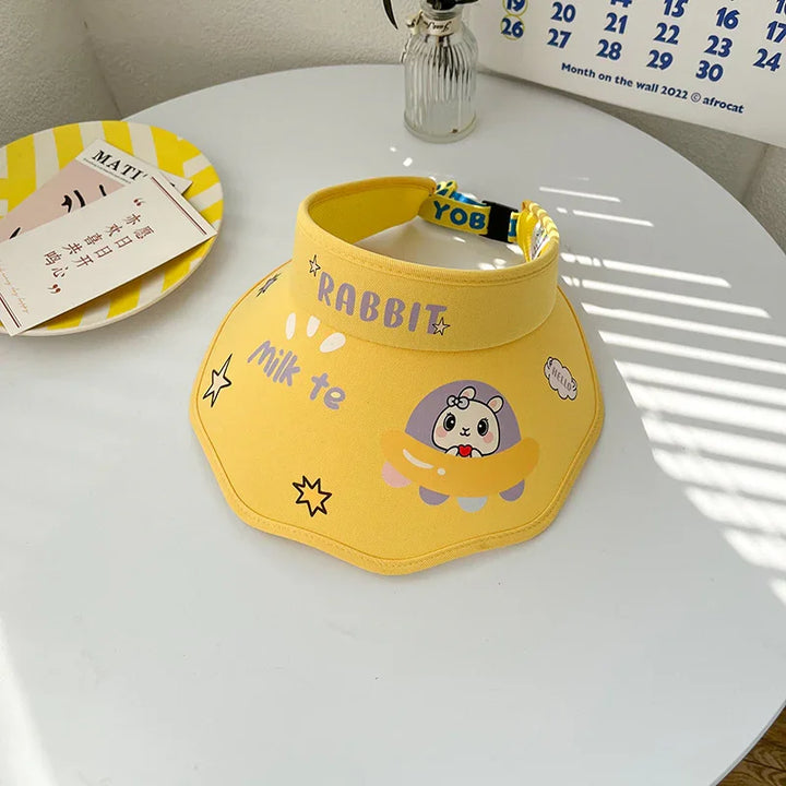 Yellow visor hat with rabbit and milk tea design, placed on a white table with calendar and plate nearby