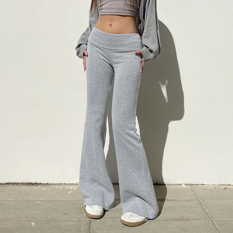 Woman wearing light gray flared sweatpants and white sneakers standing against white wall