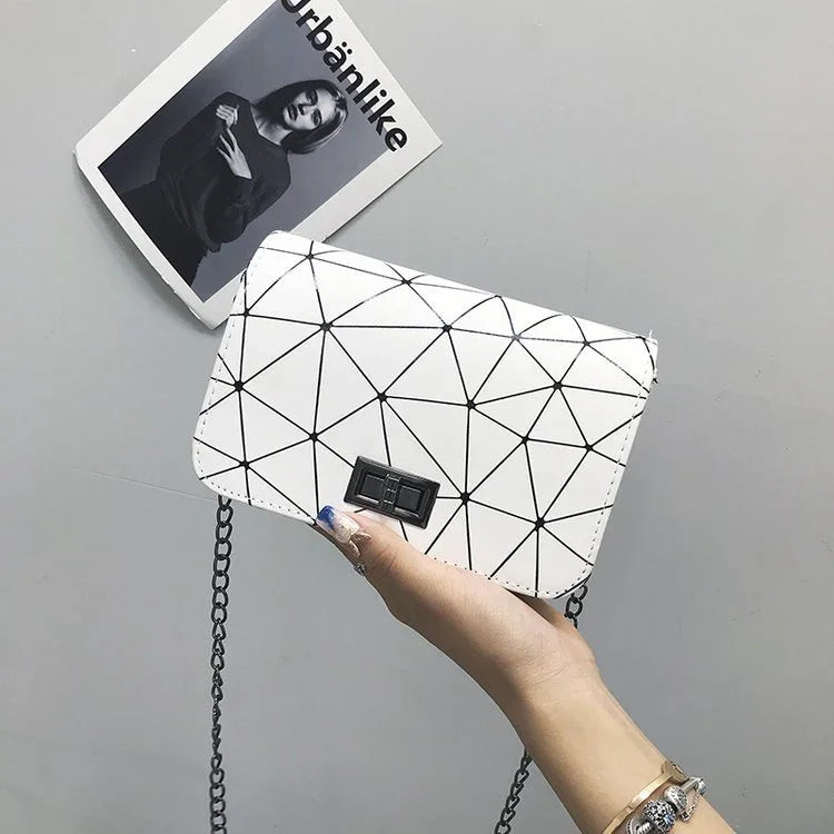 White geometric pattern crossbody purse with black chain held by hand against gray background