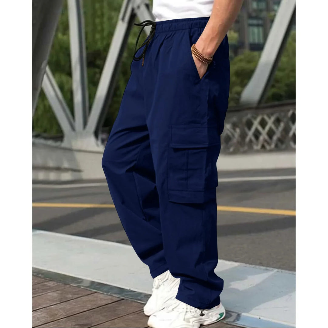 man wearing navy blue cargo pants with multiple pockets and white sneakers on urban bridge