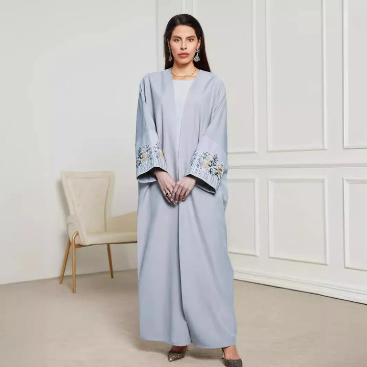 Woman wearing light gray abaya with floral embroidery on sleeves standing in minimalist room
