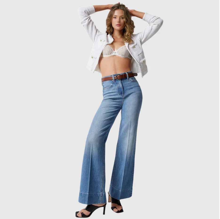 Fashion model wearing white cropped jacket, lace bralette, wide-leg blue jeans with brown belt, black heels