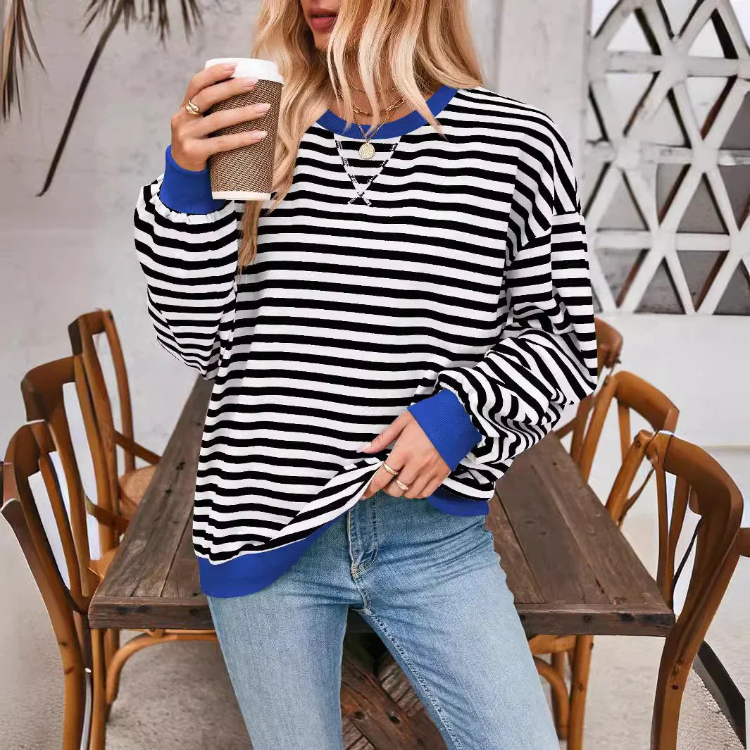 Woman wearing black and white striped sweater with blue cuffs and neckline, holding coffee cup in casual cafe