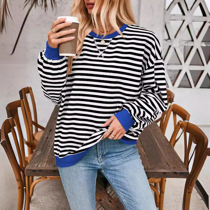 Woman wearing black and white striped sweater with blue cuffs and neckline, holding coffee cup in casual cafe