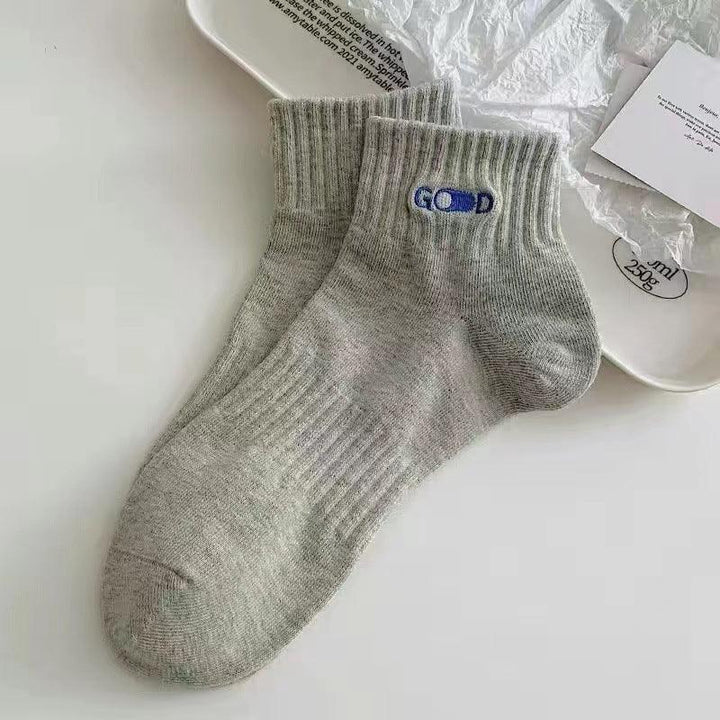 Pair of light grey ankle socks with ribbed cuffs and a blue embroidered pill design