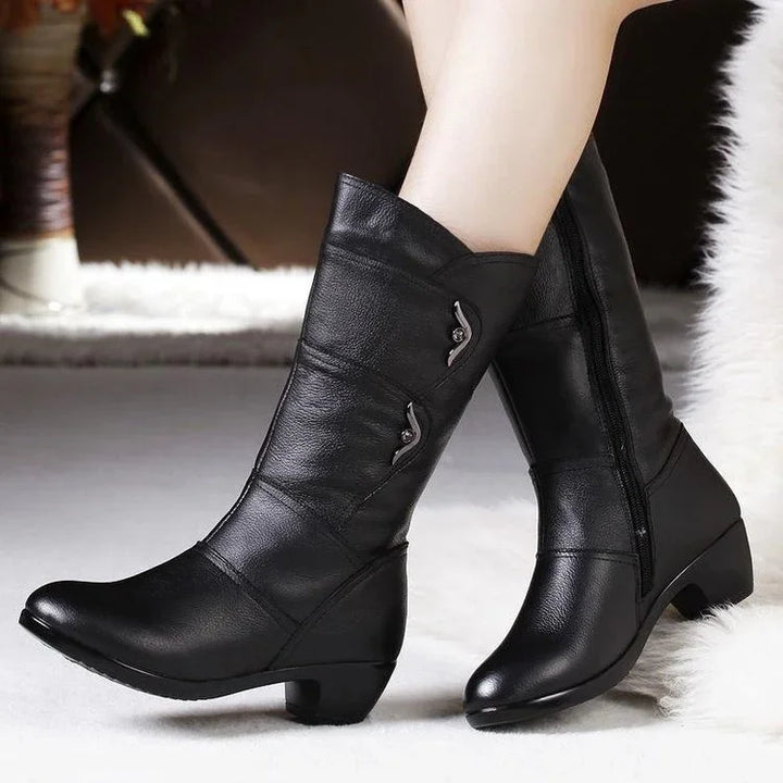 Black mid-calf leather boots with decorative metal accents and low heels on a white rug