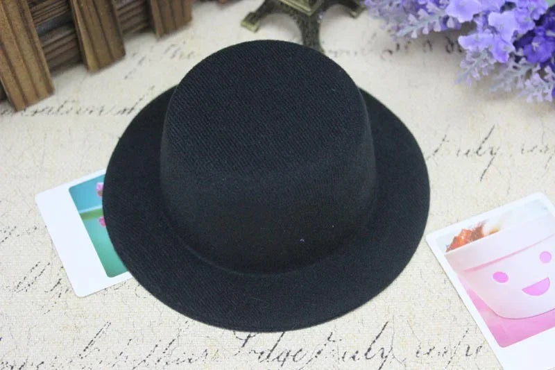 Black felt round hat with wide brim on textured fabric background with purple flowers and small photos