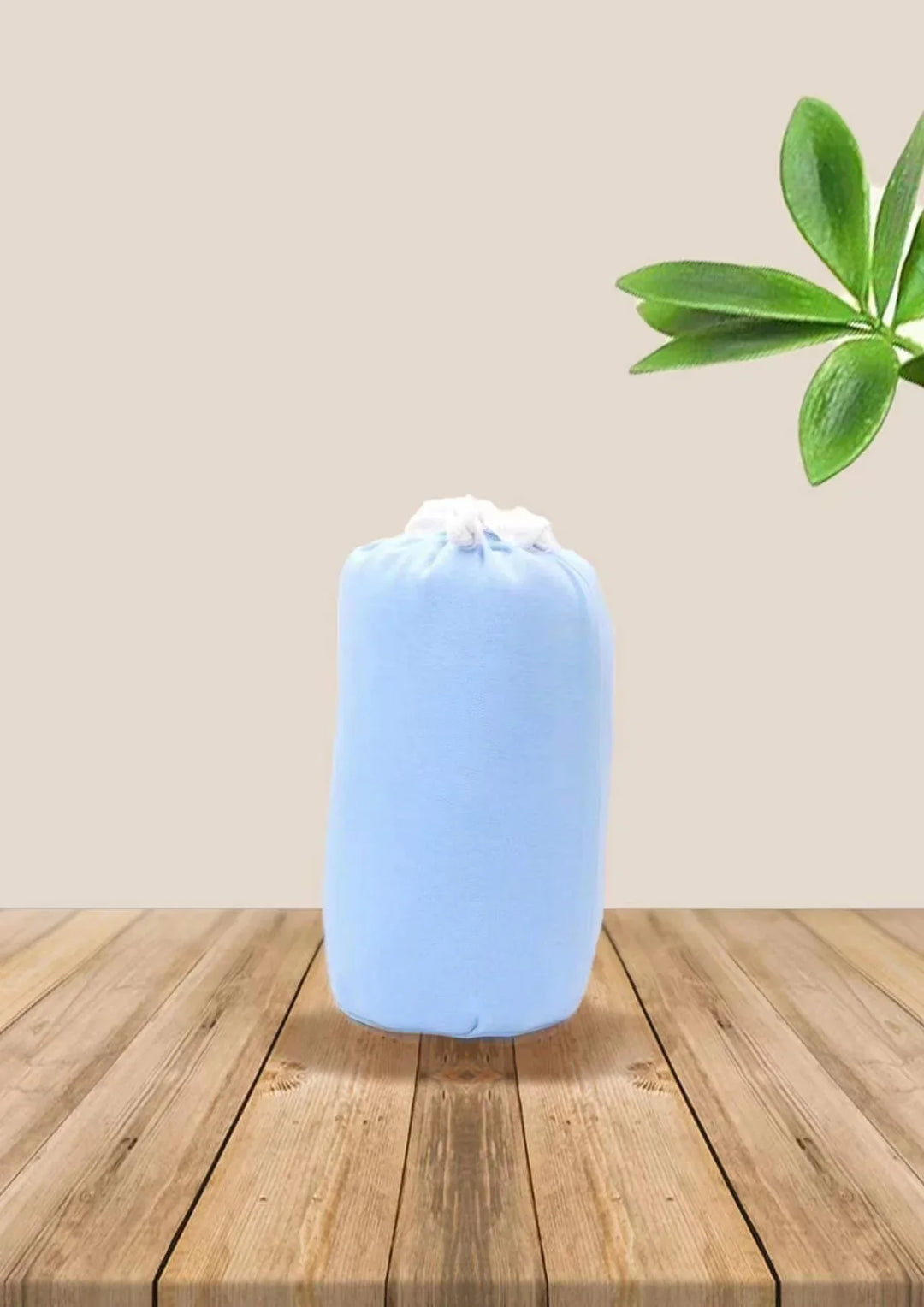 Light blue fabric bundle with drawstring, placed on wooden surface near green leaves