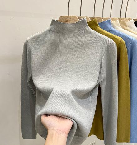 Hand holding soft gray turtleneck sweater with mustard yellow, blue, and beige sweaters hanging on wooden hangers
