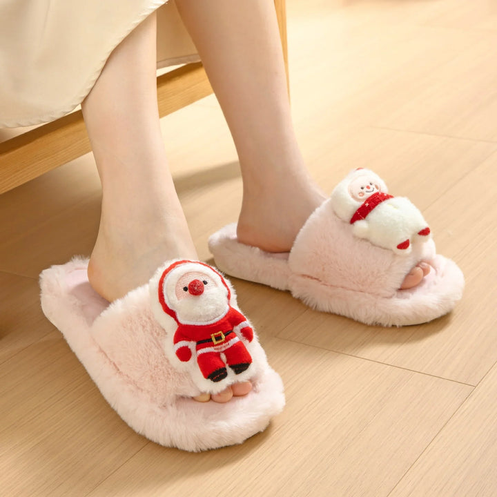 Feet wearing pink fuzzy slippers with plush Santa Claus and snowman decorations on wooden floor